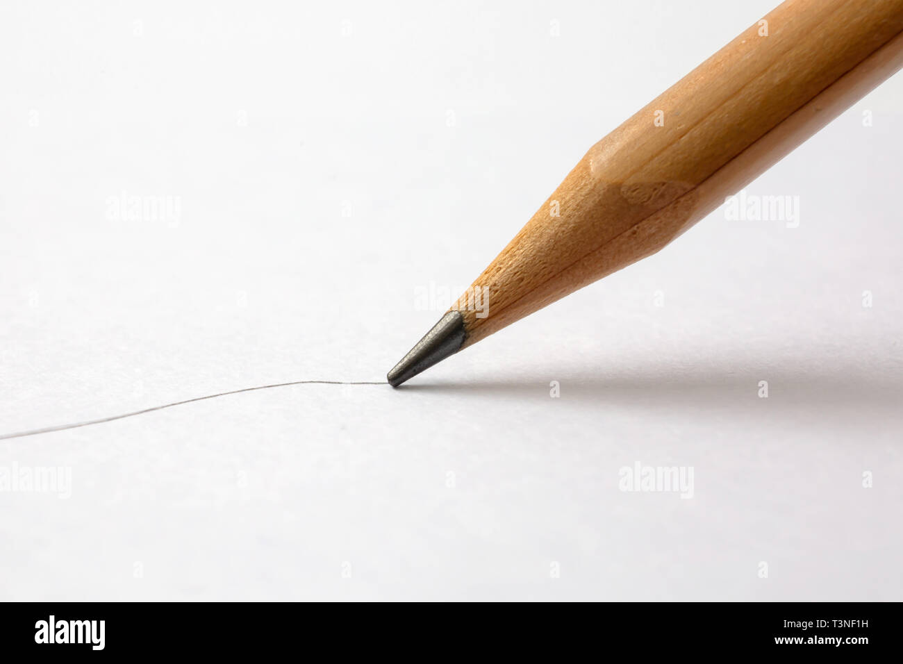 A closeup view of a black pencil drawing a line on a textured paper surface. Stock Photo