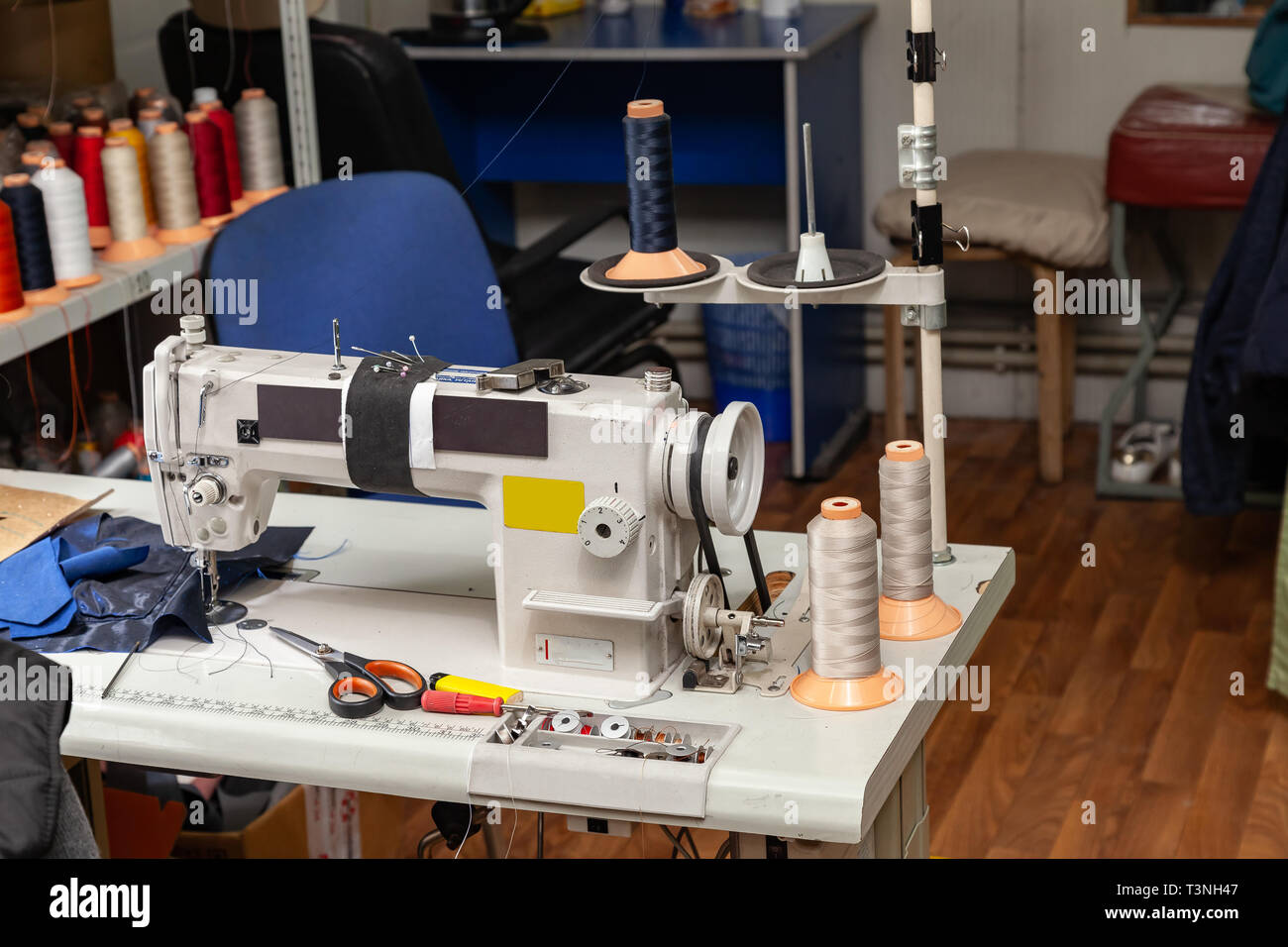 White electric industrial sewing machine in a workshop for sewing and working with fabrics. Stock Photo