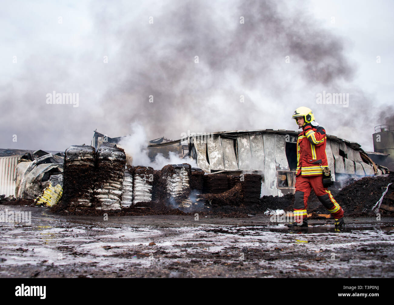 Roggendorf, Germany. 11th Apr, 2019. A firefighter walks along burnt pallets with bark mulch during a major fire in a peat factory. Several warehouses and production halls have gone up in flames there. Credit: Daniel Bockwoldt/dpa/Alamy Live News Stock Photo