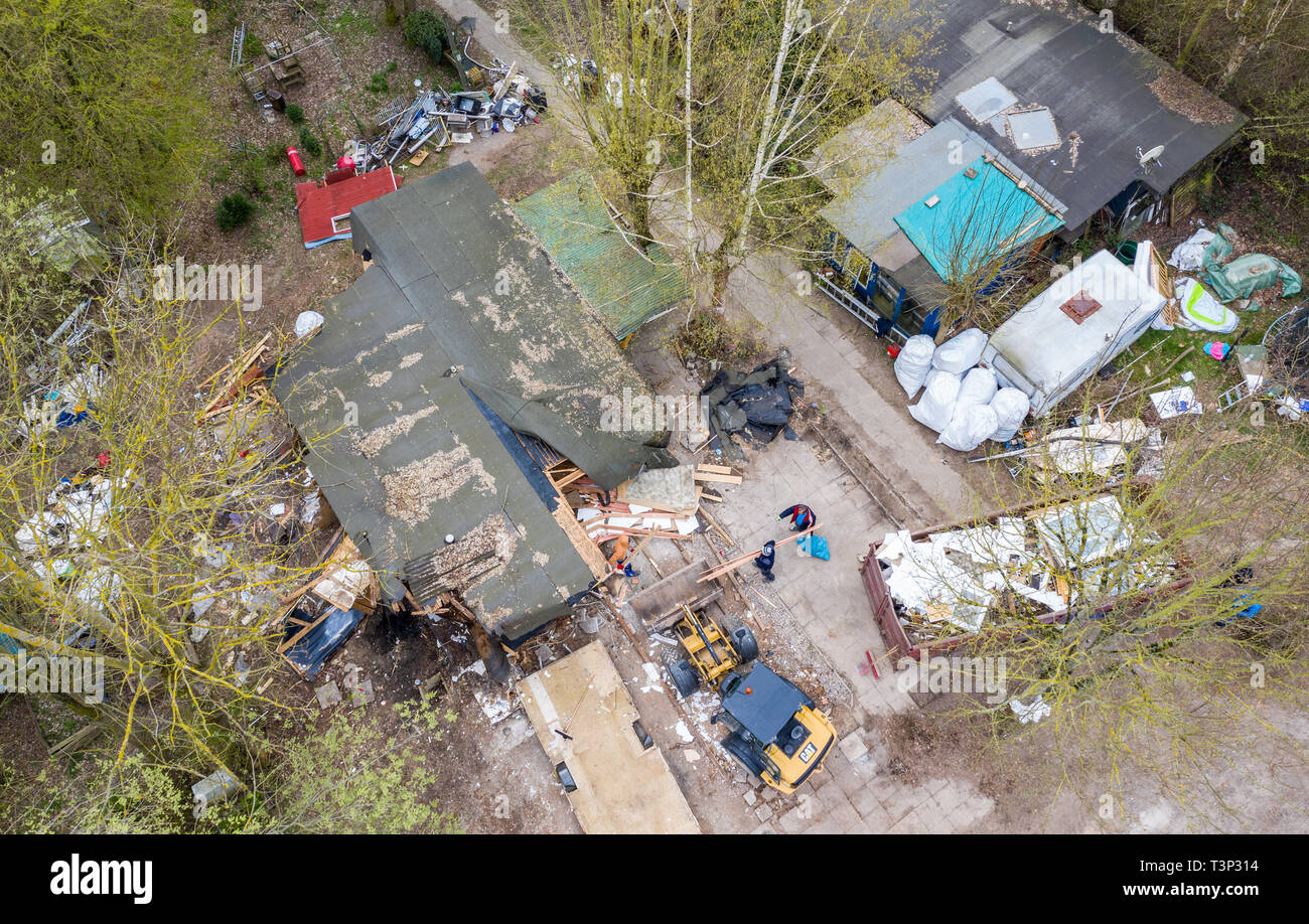 North Rhine-Westphalia, Lügde, Germany. 11 April 2019. An excavator stands in front of the partly demolished plot of land of the alleged perpetrator at the camping site Eichwald in the district Elbrinxen and demolishes the complete complex. (recorded with a drone). The campsite operator has the crime scene torn down. Children had been abused on the campsite in the district of Lippe. Photo: Guido Kirchner/dpa Stock Photo