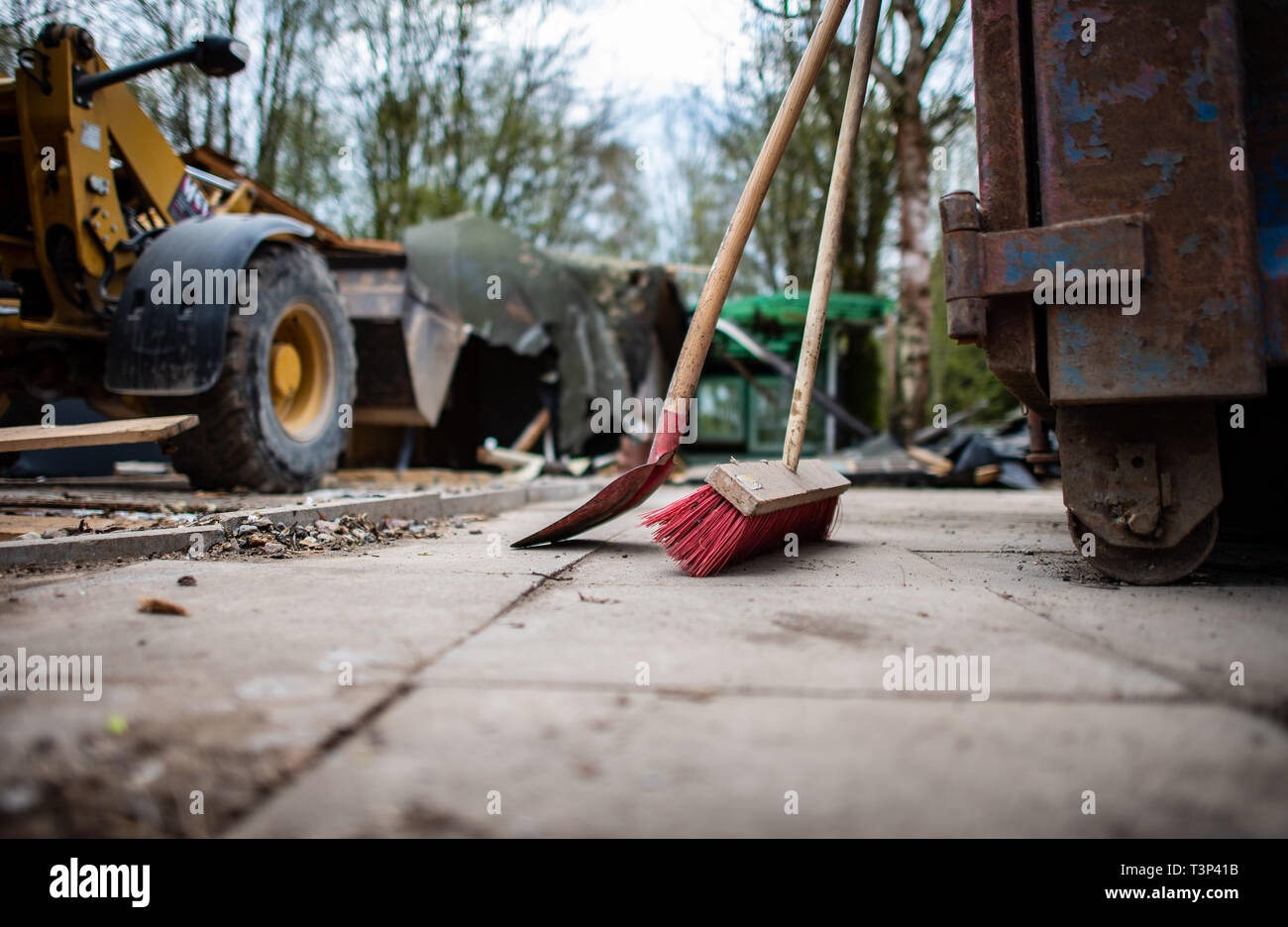 11 April 2019, North Rhine-Westphalia, Lügde: A broom, a shovel and an excavator stand in front of the partly already demolished plot of land of the alleged perpetrator at the camping site Eichwald in the district Elbrinxen. The campsite operator has the crime scene demolished, where several children were abused and filmed. The demolition work will continue until the weekend due to the large quantity. Photo: Guido Kirchner/dpa Stock Photo