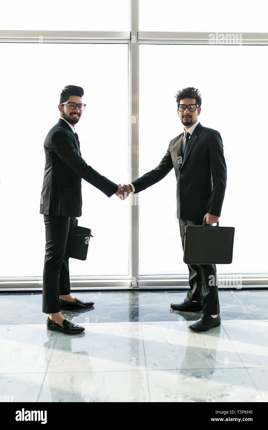Full length side view of businessmen shaking hands in office building ...