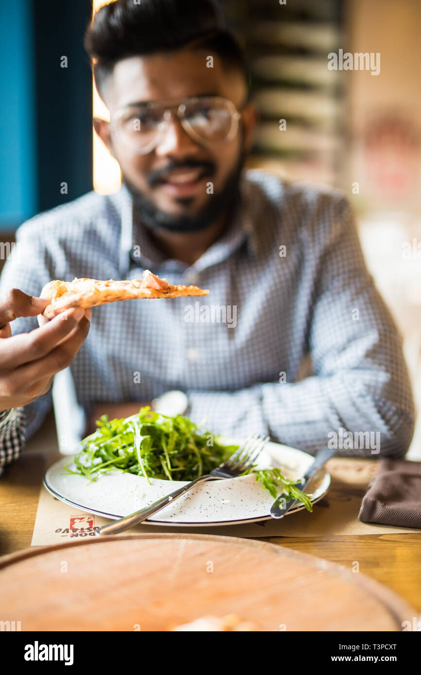 Handsome man holding and eat piece pizza and salad in cafe Stock Photo