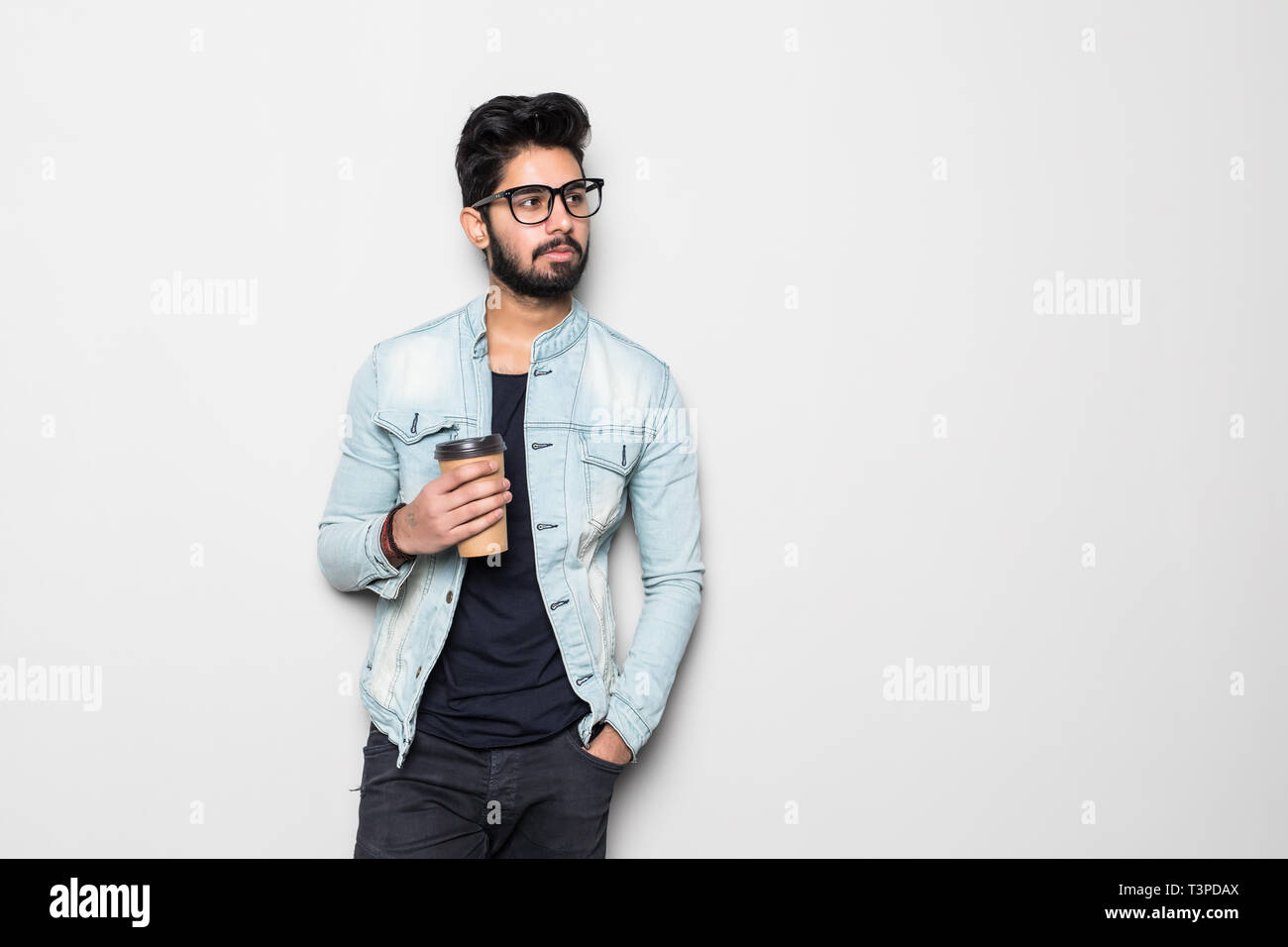 Indian guy drinking coffee. Asian standing on plain background with shadow and copy space. Handsome male model. Stock Photo