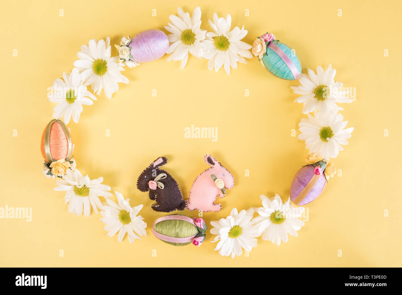 Wreath of daisies, Easter eggs, and Easter bunnies on solid pastel yellow background Stock Photo