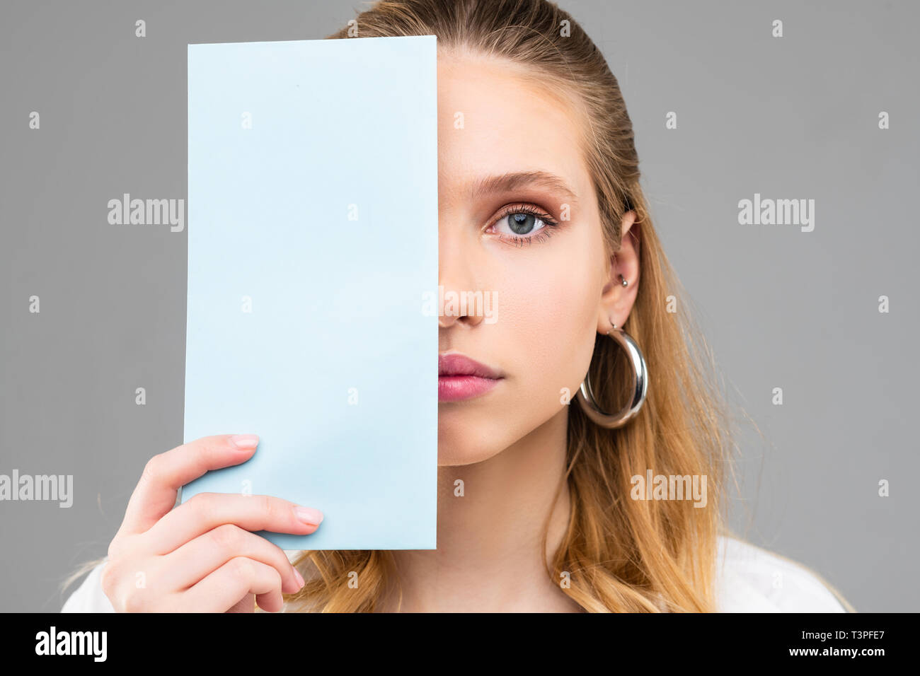 Flawless adult woman with thick earrings and light hair closing part of her face Stock Photo