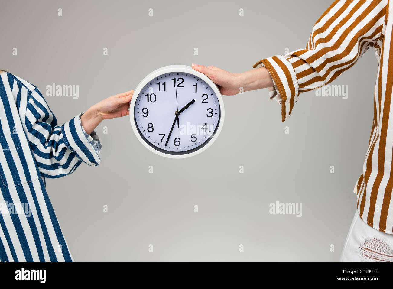 Women in oversize striped outfits carrying plain wall clock Stock Photo