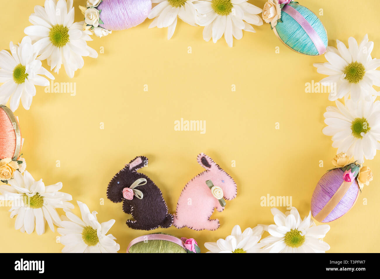 Easter eggs, bunnies, and daisies in wreath on solid pastel yellow background Stock Photo