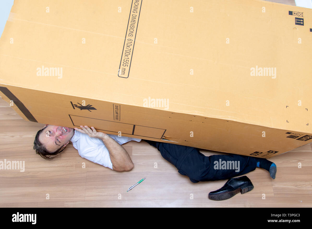 The unhappy man lying under a big box. Large cardboard fall down at the postman. Stock Photo