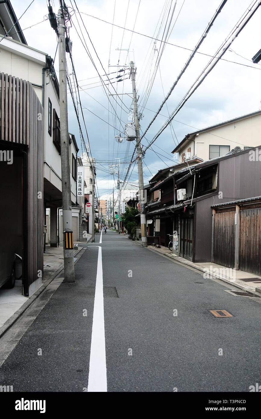 Narrow rural street in city of Kyoto with old traditional japanese buildings made of wood and crooked power poles Stock Photo
