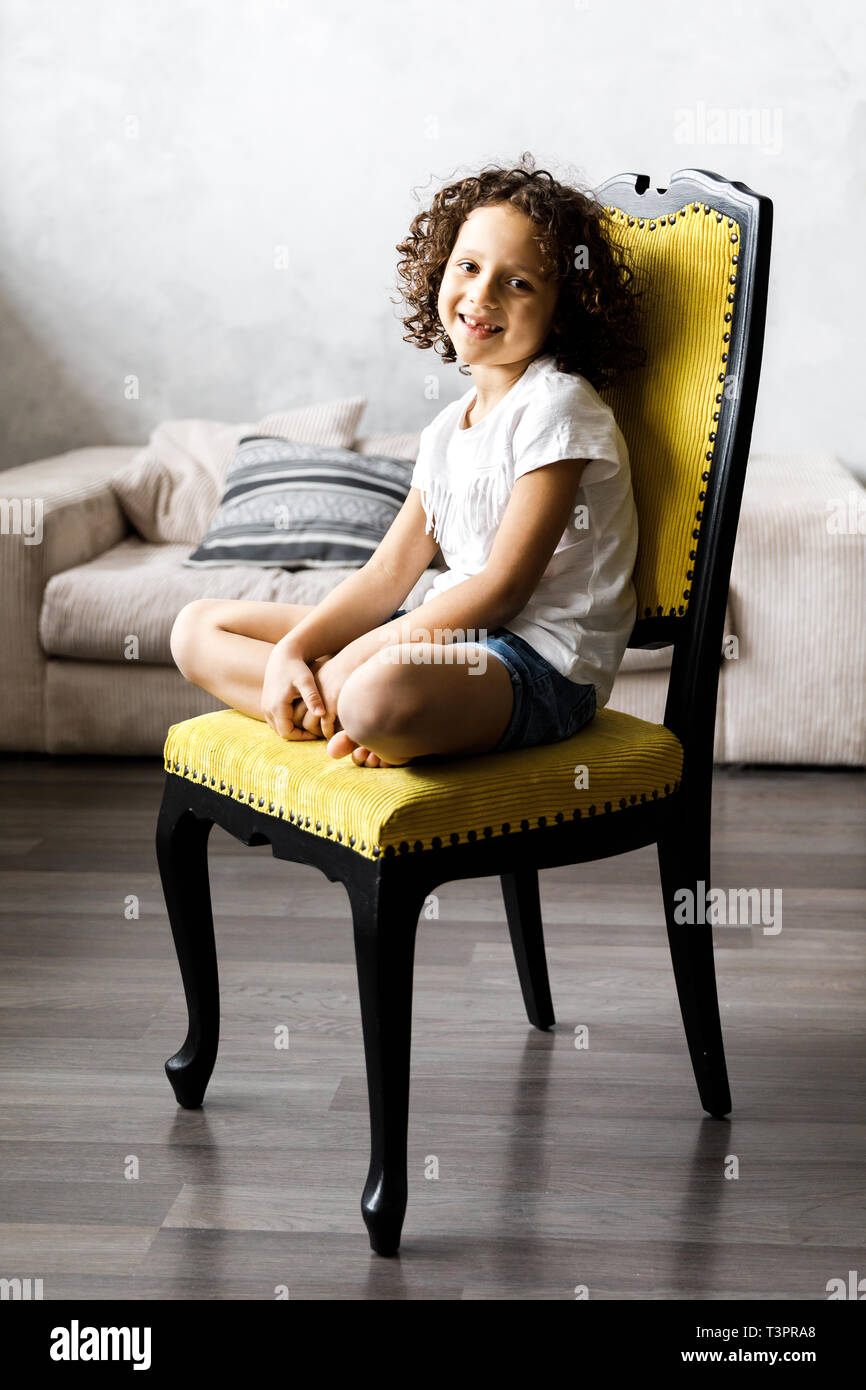 A pretty cute little girl with curly hair sitting on the chair and ...