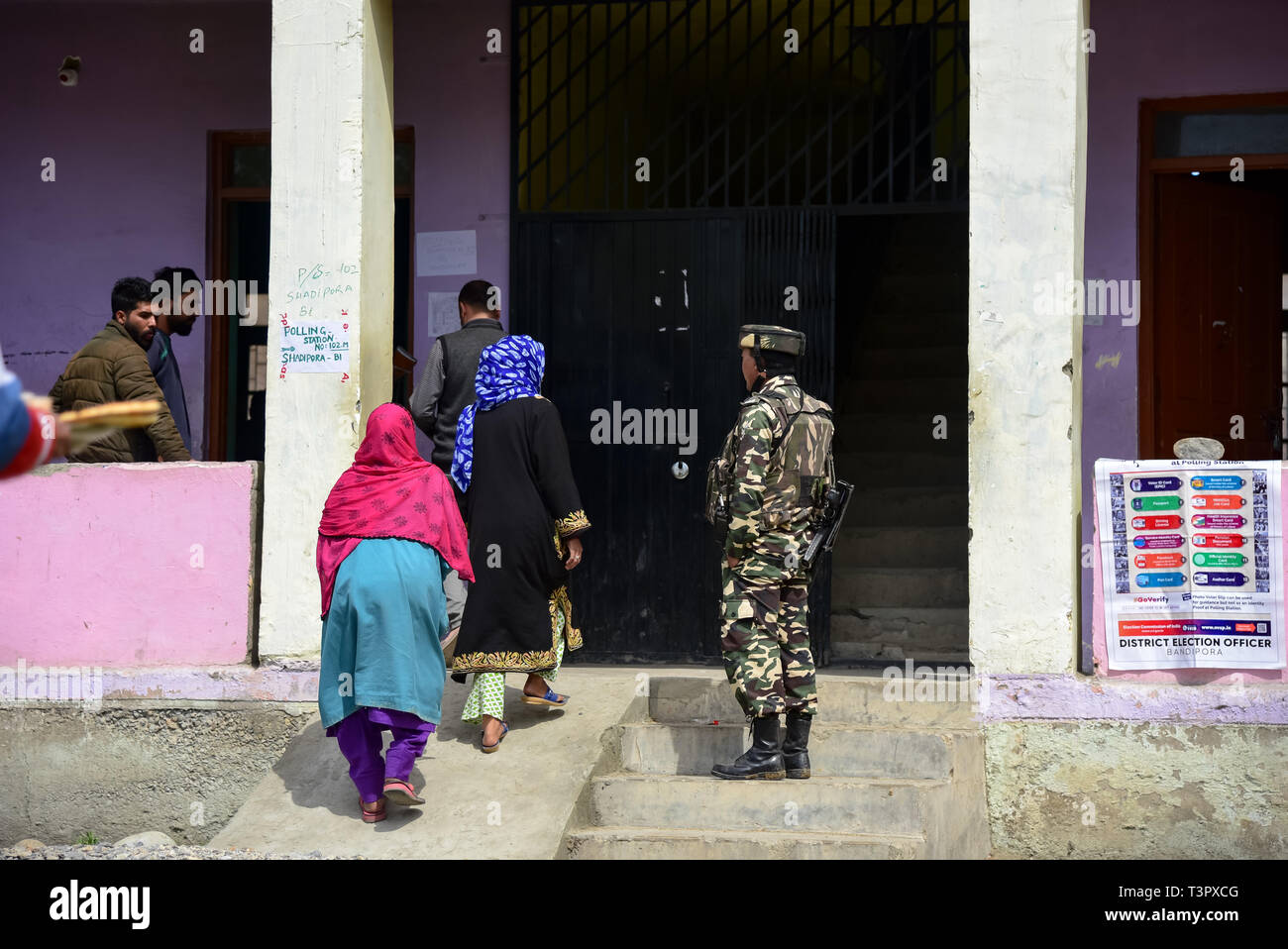Kashmiri voters seen entering a polling station past Indian army man standing guard outside polling station at Shadipora. Voting began for two parliamentary seats in the Indian Kashmir amid tight security and a boycott call by separatists. Armed police and paramilitary soldiers in riot gears guarded polling stations and nearby roads. Stock Photo
