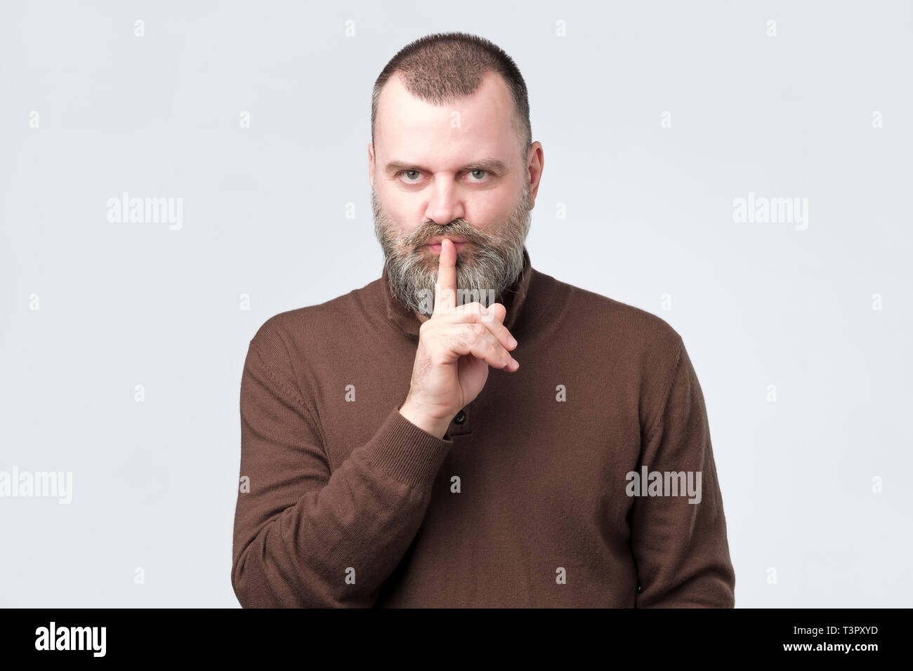 Mature man with beard in brown shirt making silence gesture Stock Photo