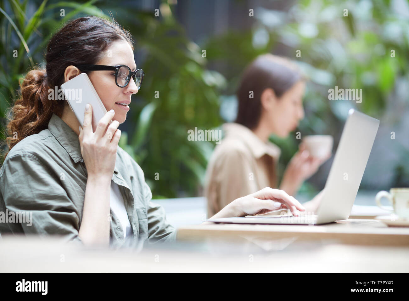 Freelance manager talking on phone while using laptop Stock Photo