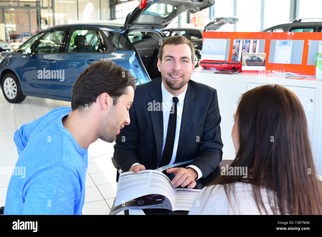 young couple buying a new car in the showroom of a car dealership - signature sales contract with seller Stock Photo