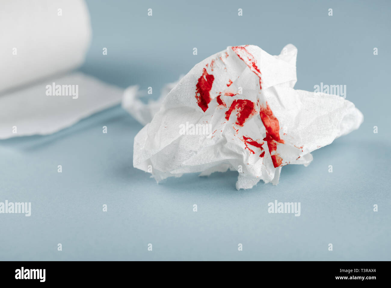 Hemorrhoids, treatment health problems. Toilet paper with the blood drops on the blue background Stock Photo