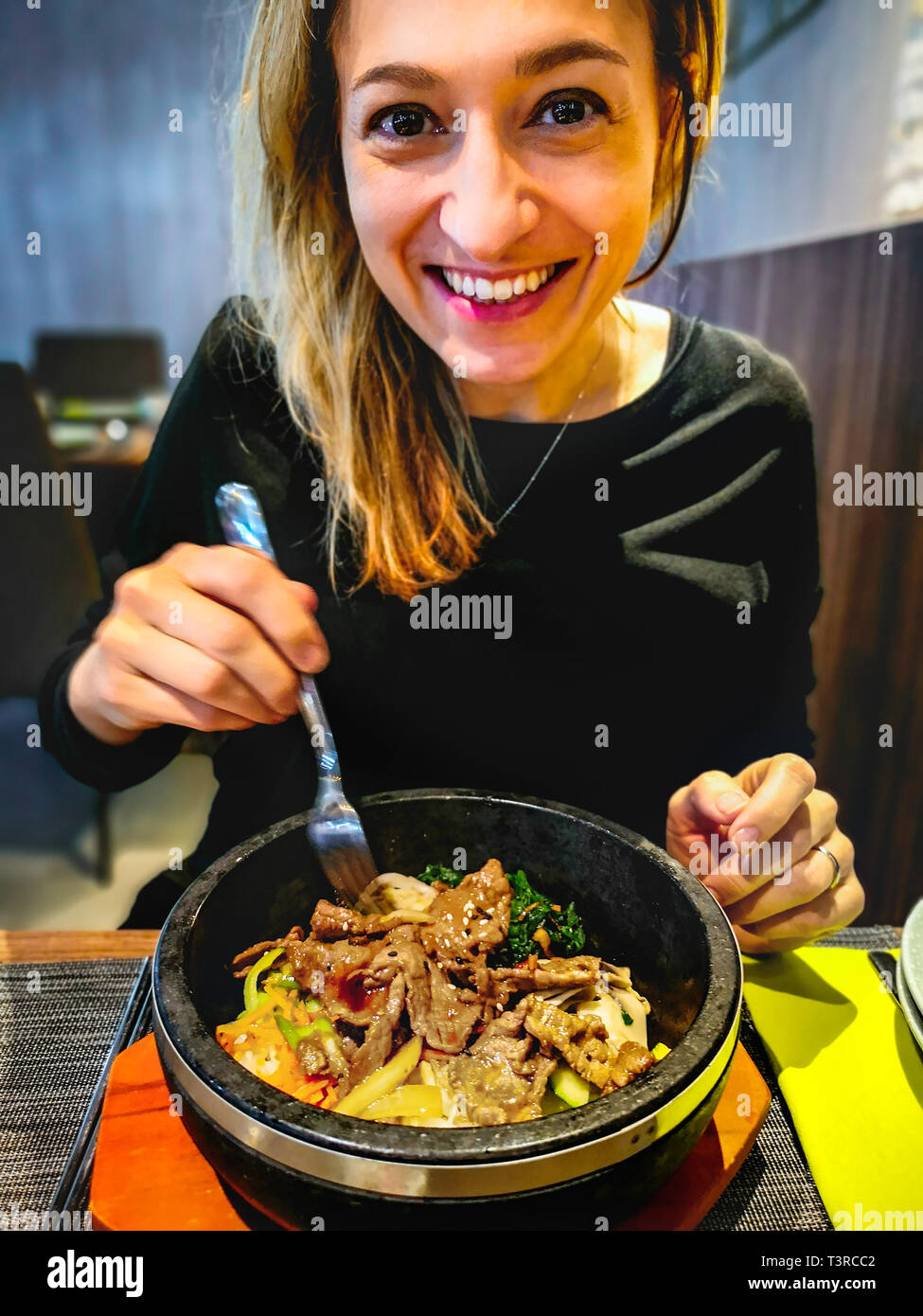 korean bibimbap served in hot stone dolsot pot bowl eaten by caucasian smiling woman dining in korean ethnic restaurant Stock Photo