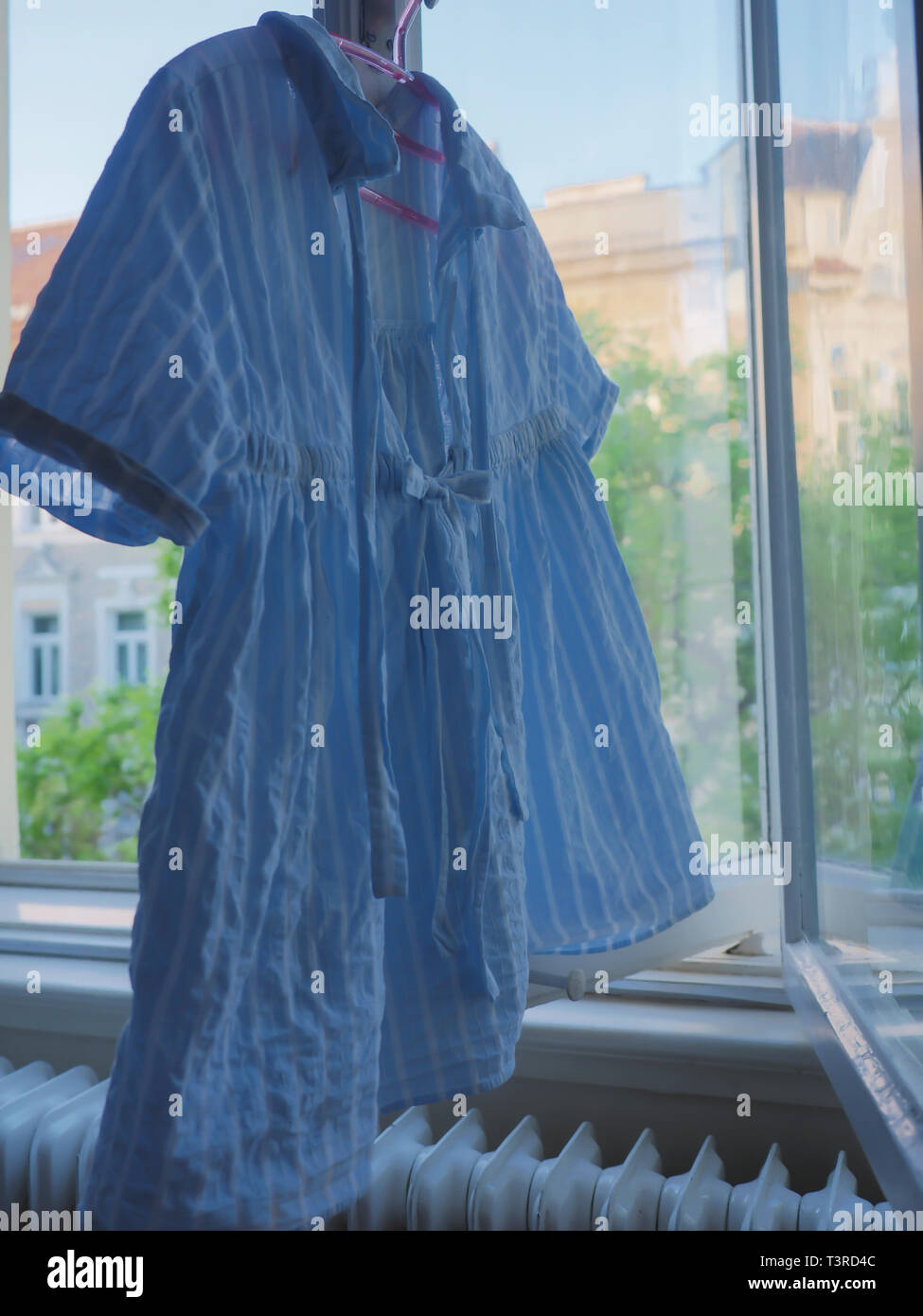 A girls blue summer shirt hanging to dry in the window Stock Photo