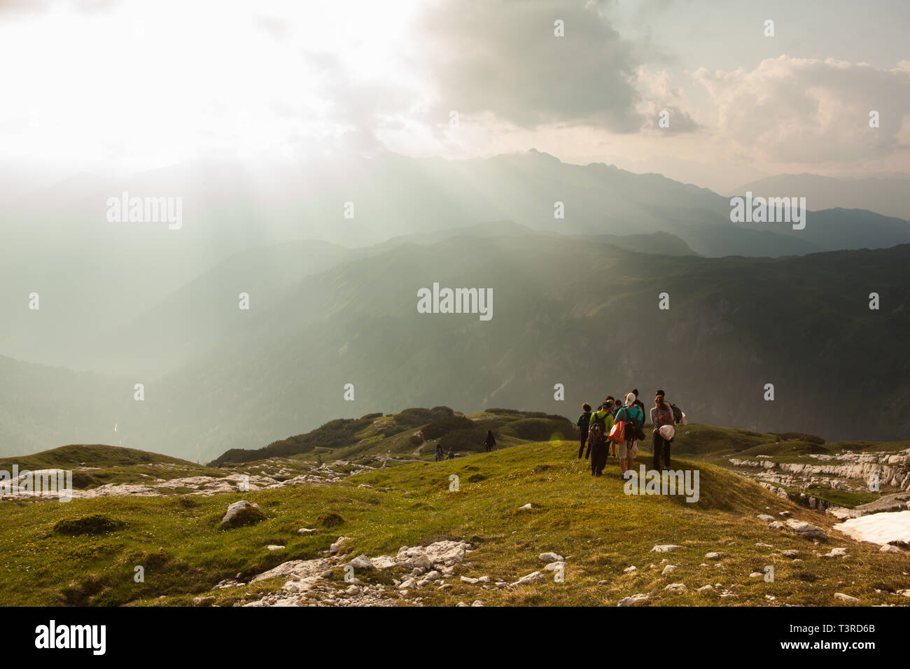 A group of summer hikers head down the mountians into the sunkissed valley, Dolomites, Italy Stock Photo