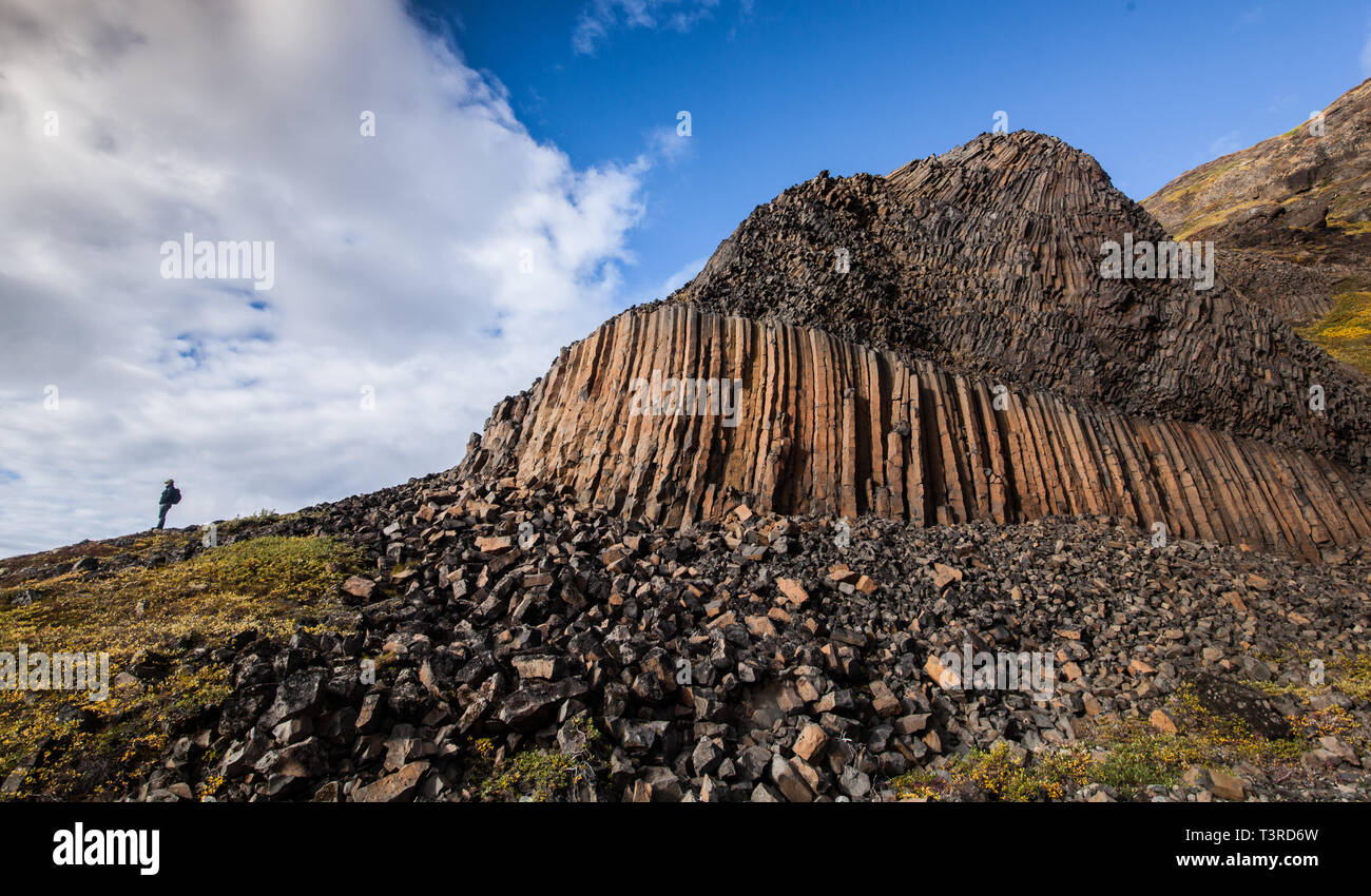 A man stands looking out on a ridge near a Basalt formation in Greenland. Stock Photo