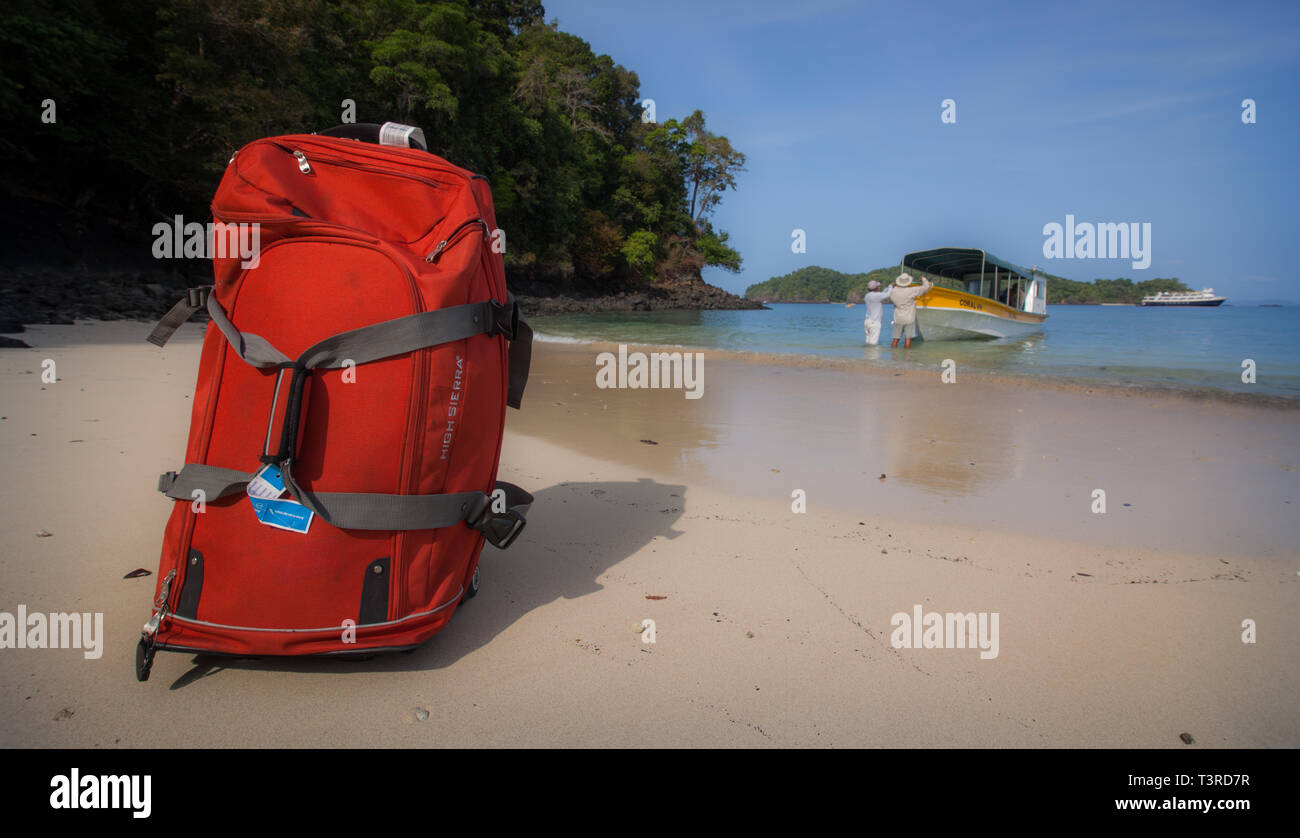 A red suitcase rests on a beach after being dropped off by a panga boat on Isla Coiba, Panama Stock Photo