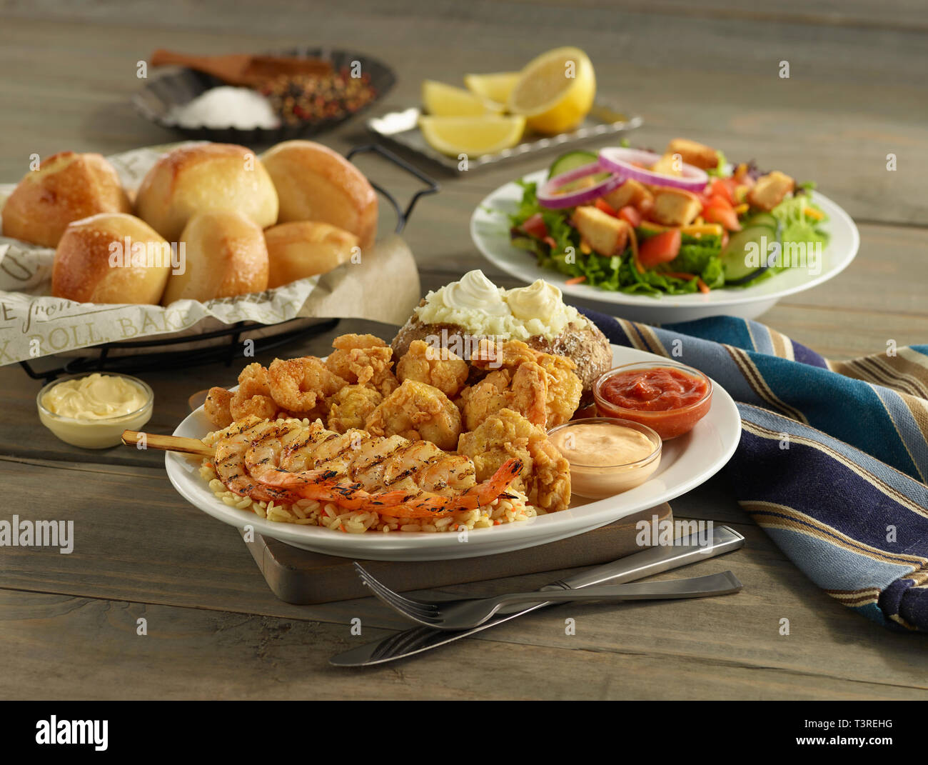Fried and grilled shrimp dinner platter with baked potato, salad, and rolls Stock Photo