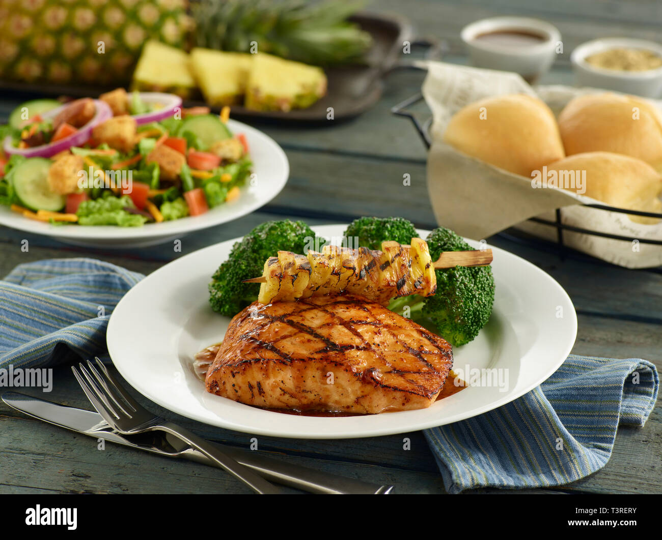 Glazed salmon filet with grilled pineapple, broccoli, salad and dinner rolls Stock Photo