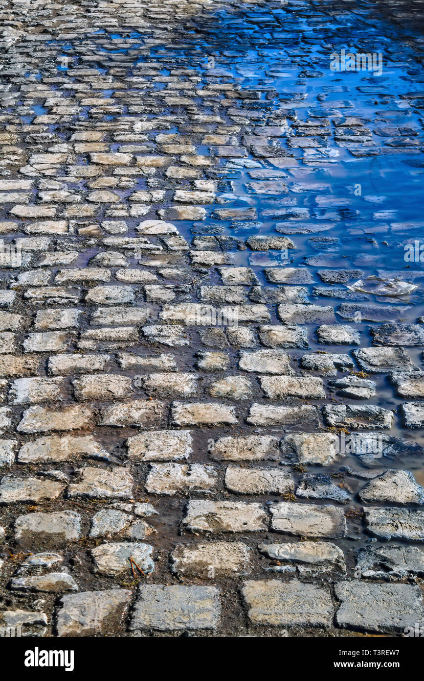 Blue spring sky reflected in the puddles on the cobblestone pavement close-up. Stock Photo