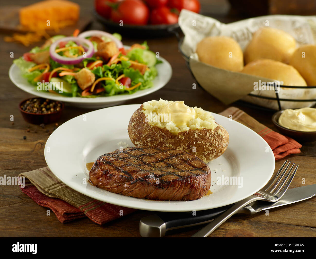 Sirloin steak with baked potato, salad, and dinner rolls Stock Photo