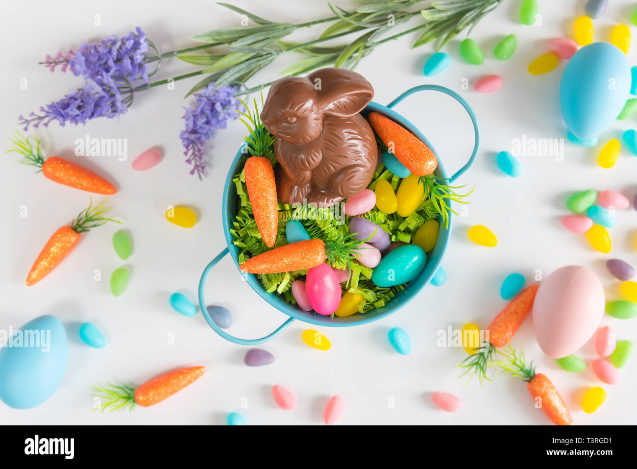 Close-up of Easter basket with chocolate bunny, mini carrots, and candy eggs on white background Stock Photo
