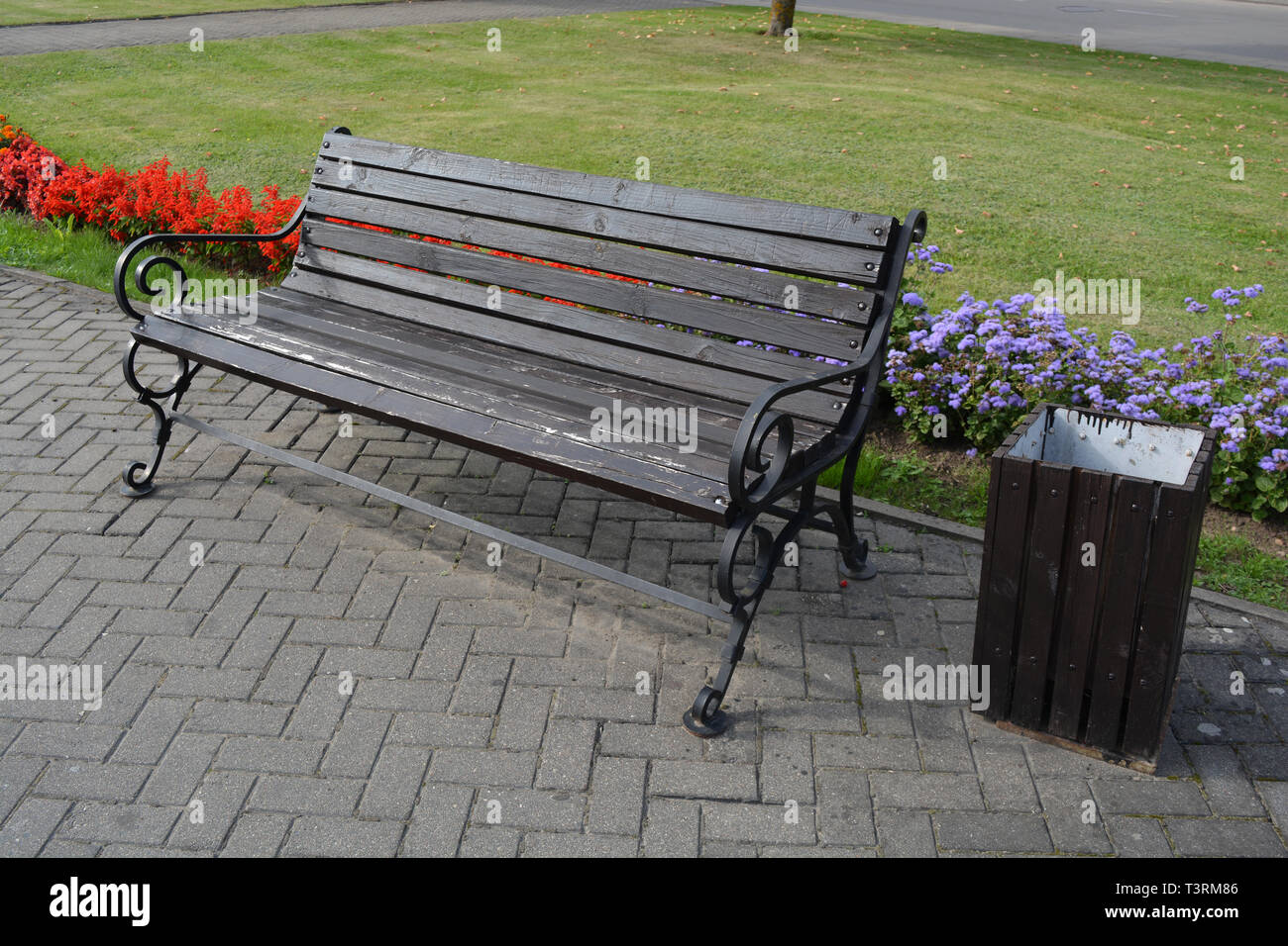 Modern wooden bench with metal frame in city street, flowerbeds and dustbin Stock Photo