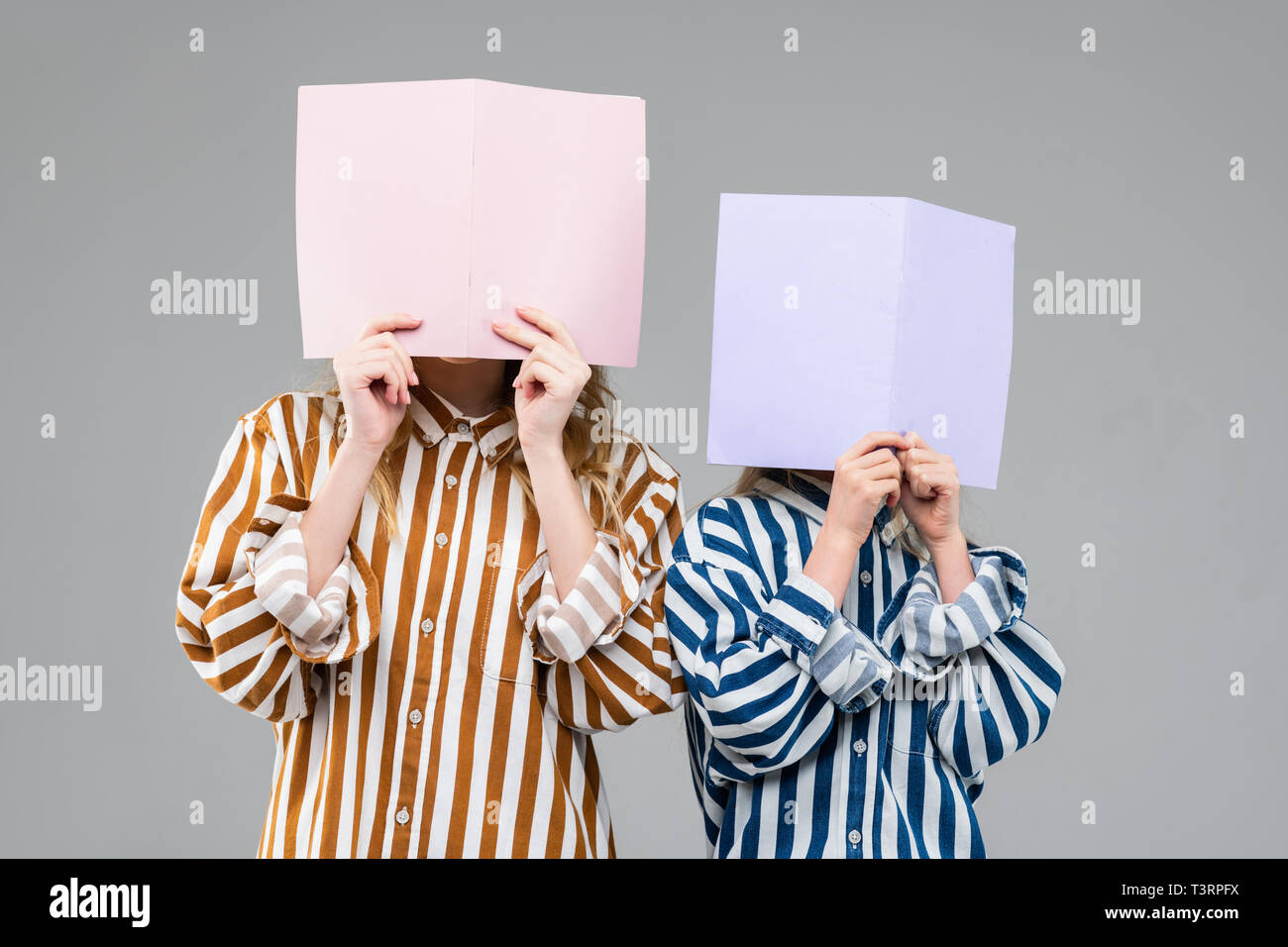 Girls in colorful striped oversize shirts covering their faces Stock Photo
