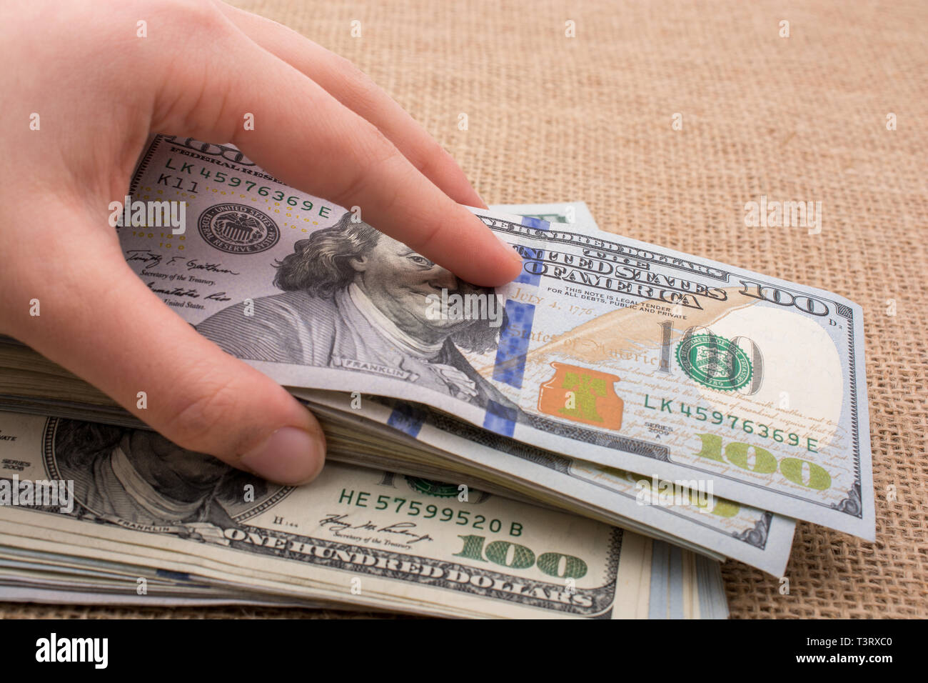 Hand holding banknote bundle of US dollar on a linen canvas background ...