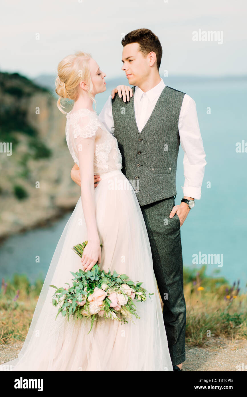 Beautiful bride and groom hug each other tender standing on the golden hill near sea Stock Photo