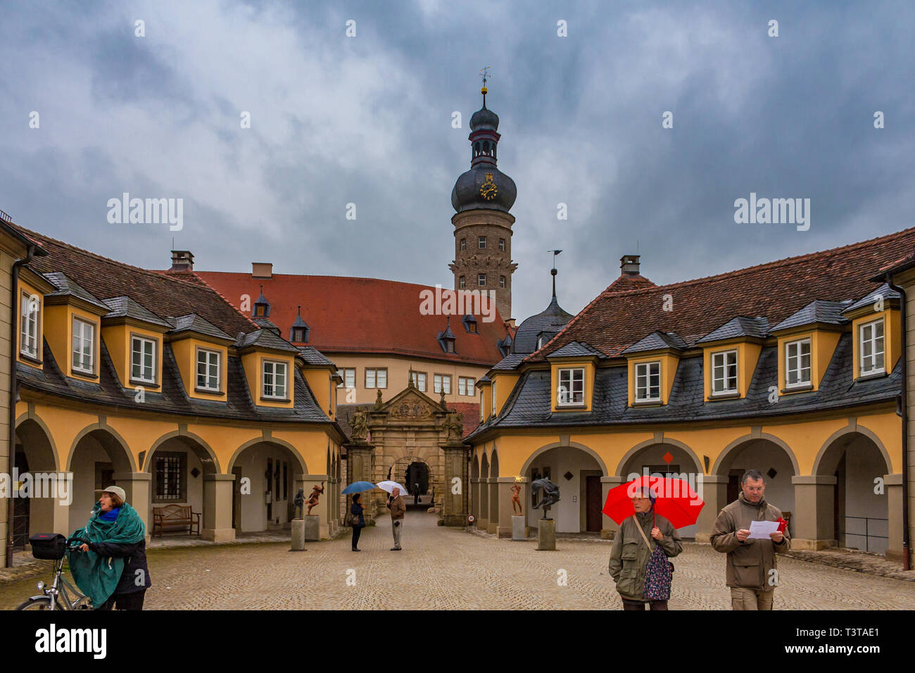 Weikersheim, Germany - MAY 2010: People with umbrellas standing in front of the cobble stoned baroque entrance to the famous Weikersheim Palace with... Stock Photo