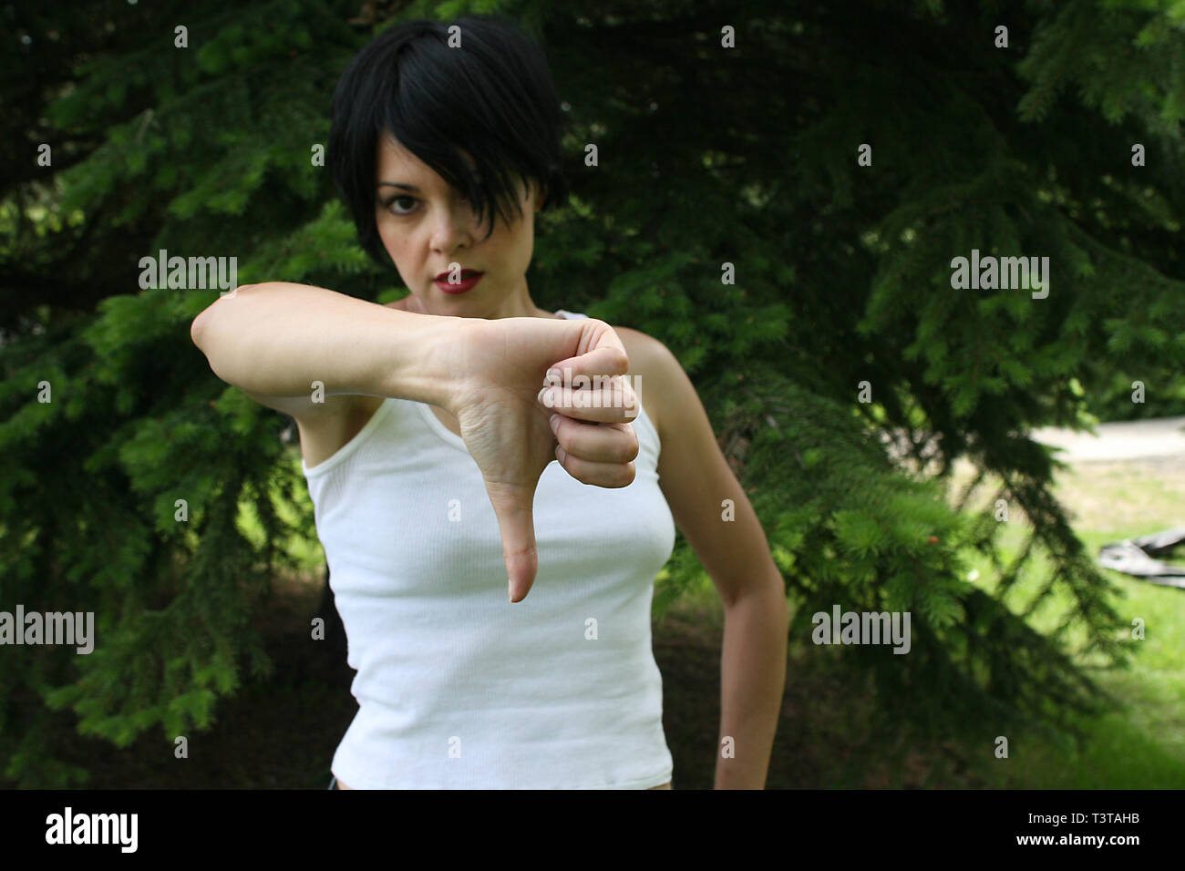 Beautiful dark haired lady with a white top making hand signals. Two thumbs down. Stock Photo