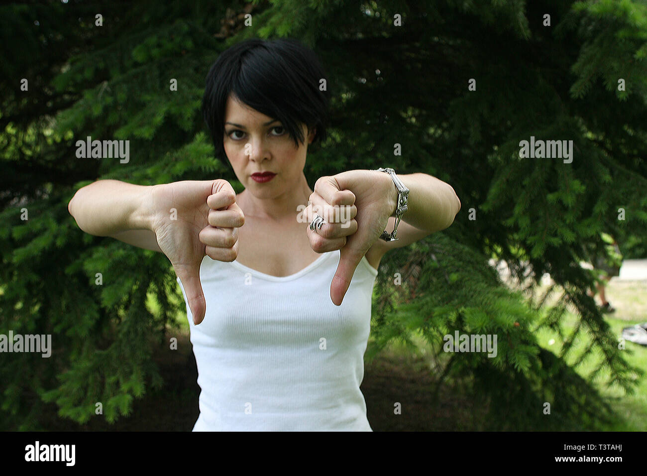 Beautiful dark haired lady with a white top making hand signals. Two thumbs down. Stock Photo
