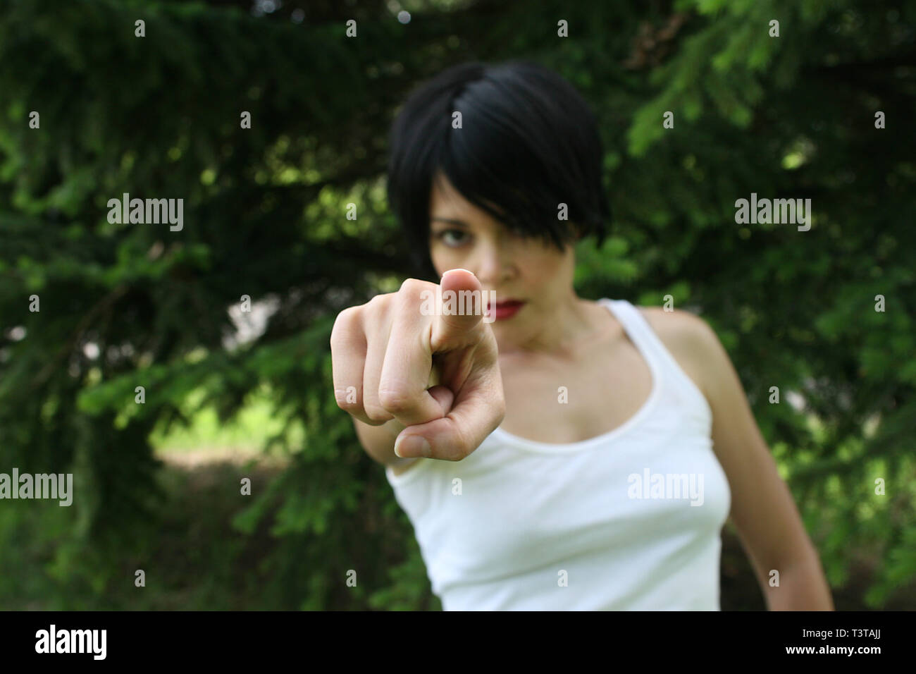 Beautiful dark haired lady with a white top making hand signals. She's pointing her finger at you. Stock Photo