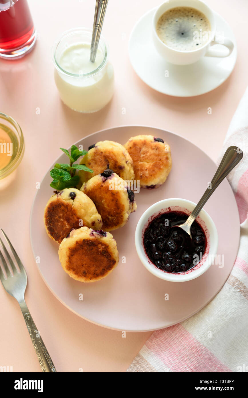 Cottage cheese pancakes with blueberry, honey, jam and coffee. Ukrainian syrniki, cottage cheese fritters or pancakes on pink wooden background. Healt Stock Photo
