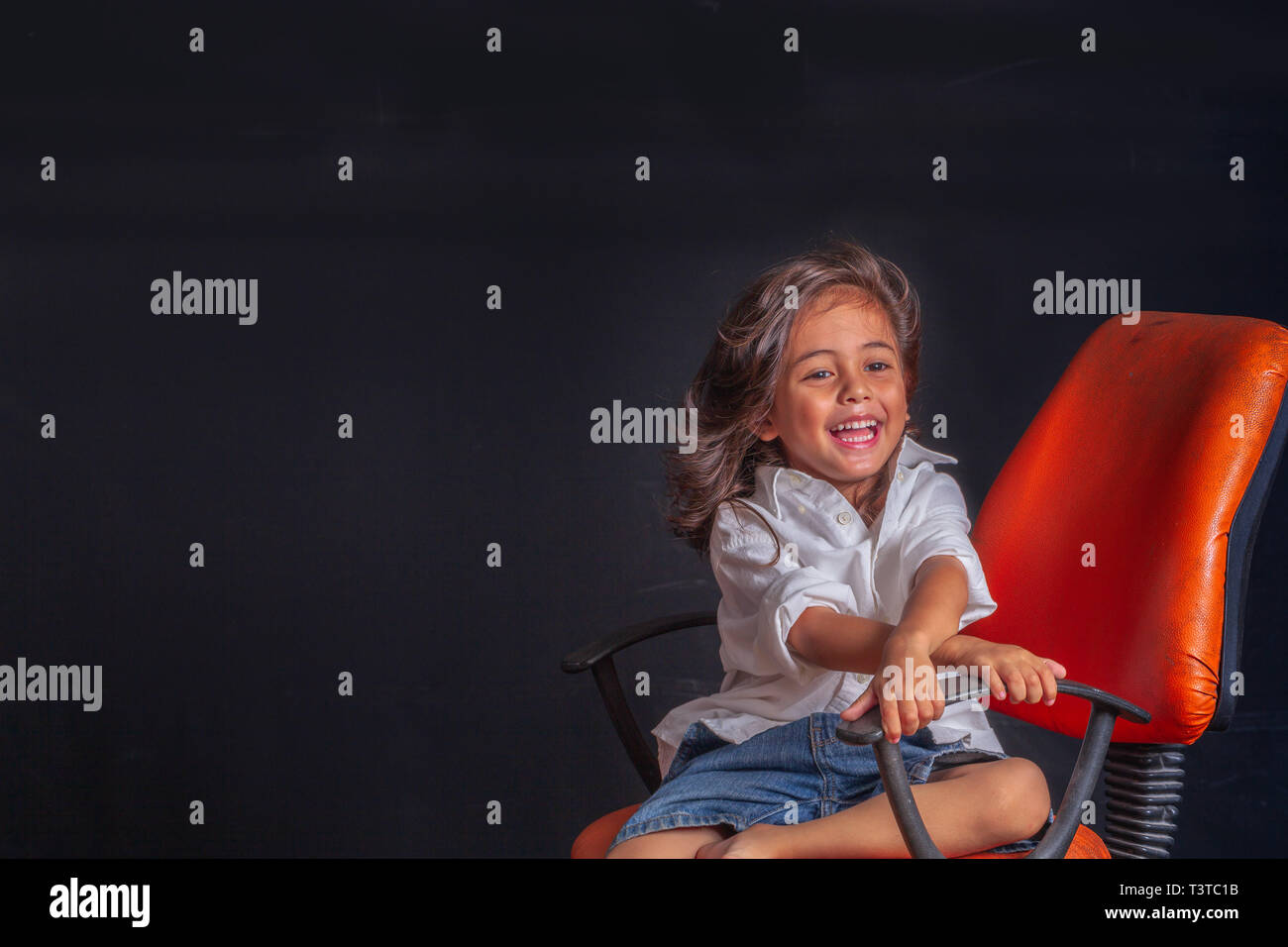 A Long Hair Boy Sitting On Orange Chair In Black Scene In Studio