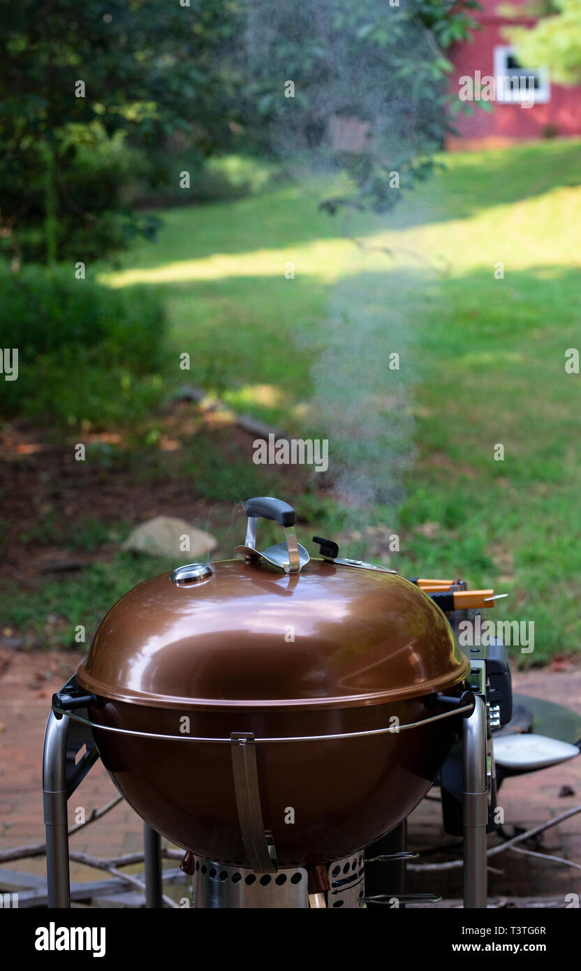 Smoking Barbecue Grill In Foreground With Lawn Trees And Red