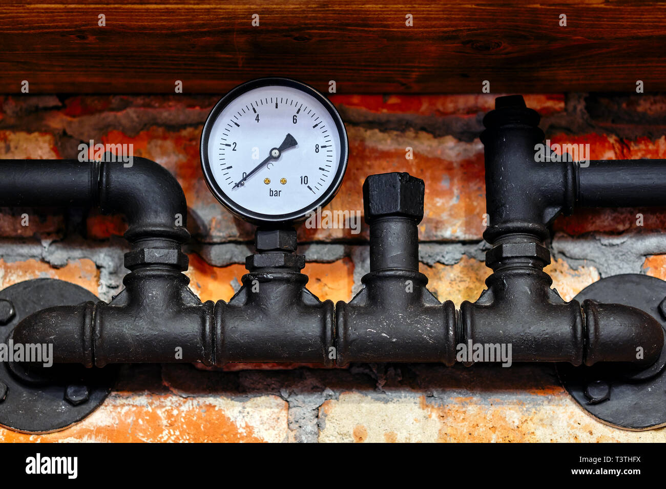 Old black pipeline pressure gauge close up against a brick wall ...
