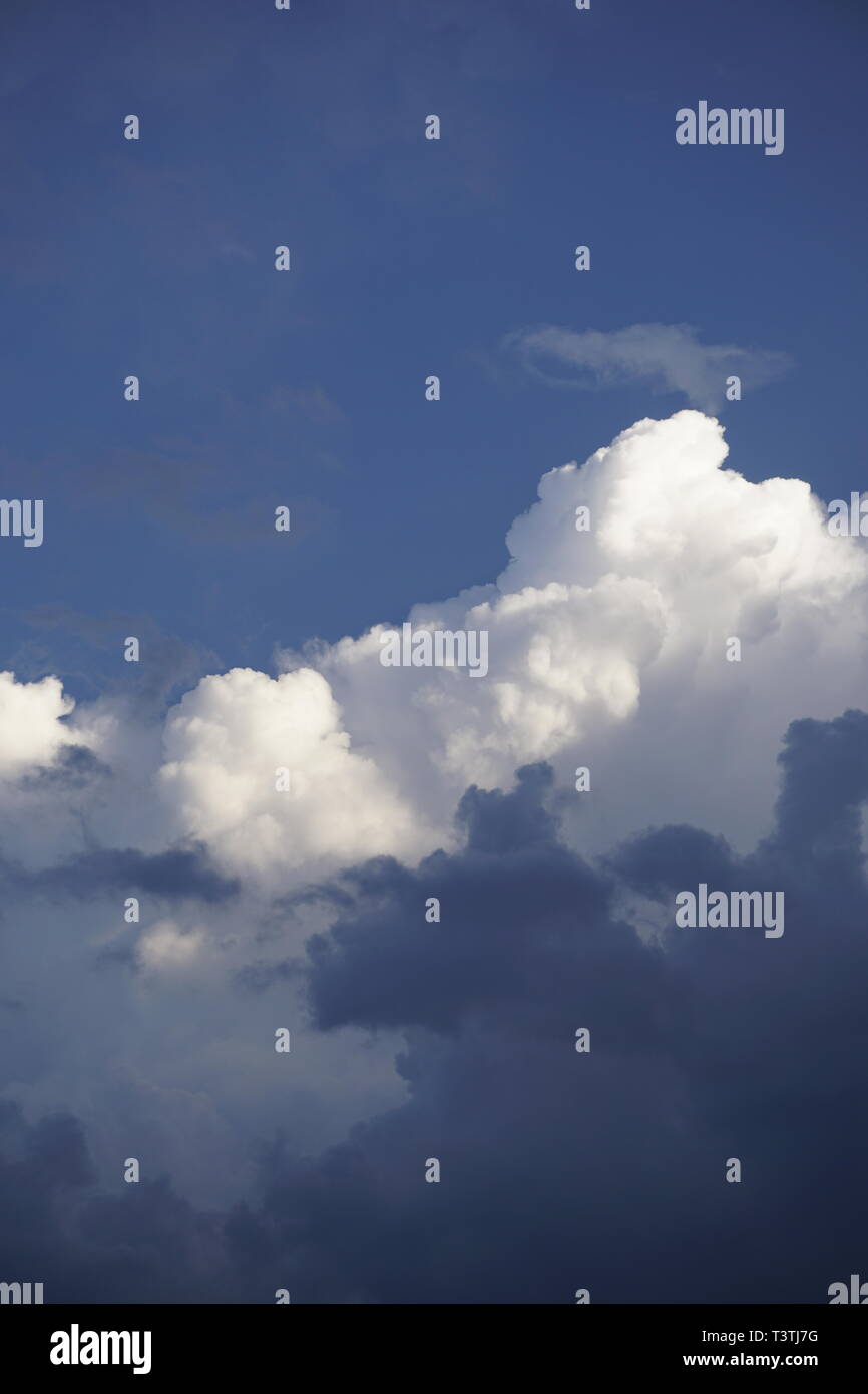 layered clouds, fluffy white and dark grey, in front of blue sky Stock Photo
