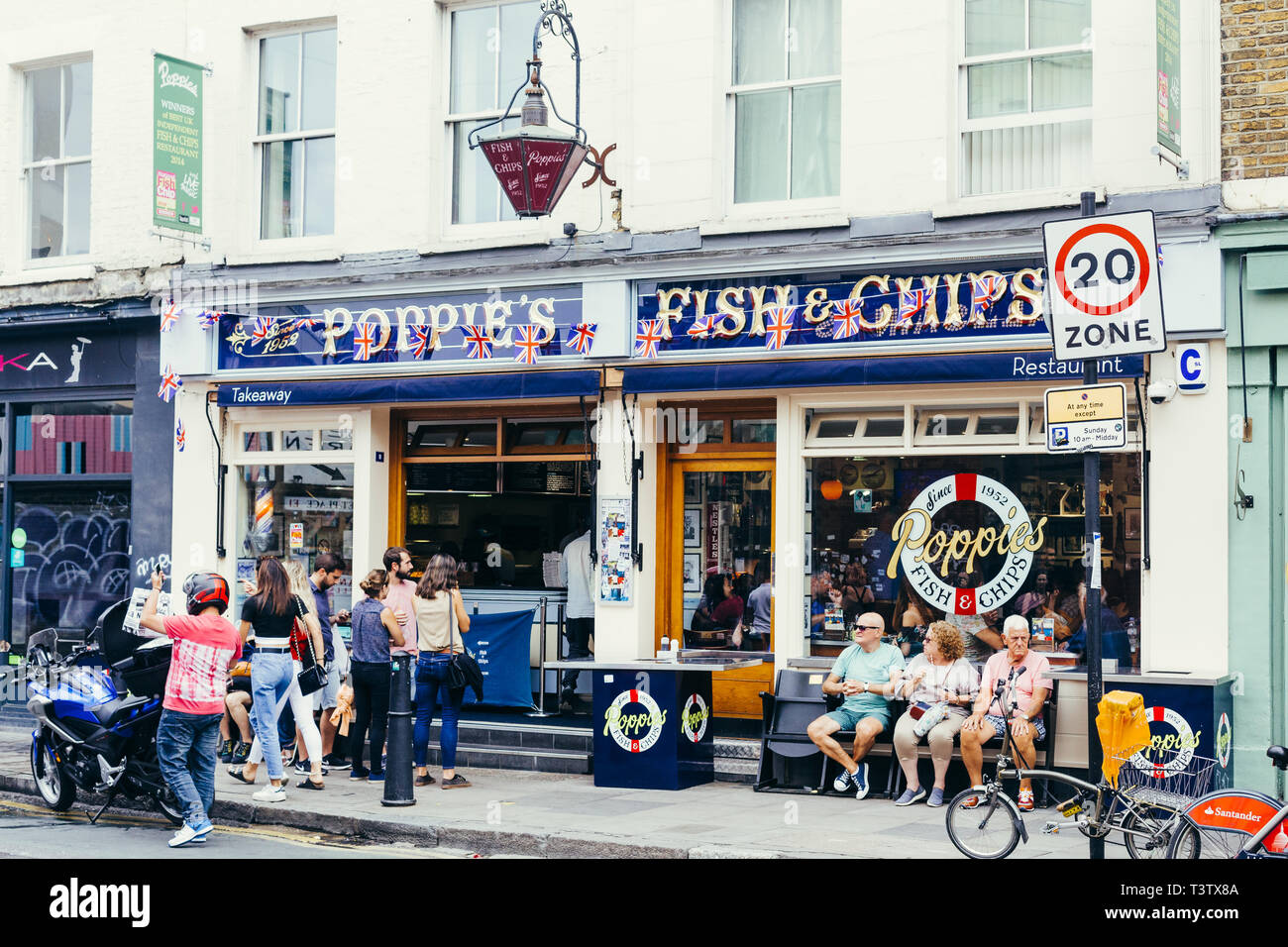 London, UK - July 22, 2018: People sitting on a bench and walking near Poppie's, famous fish & chips shop in Spitalfields, London Stock Photo
