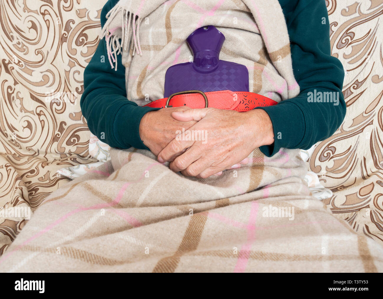 Man on sofa holding hot water bottle: energy bills, cold weather,  household bills, vulnerable pensioner, man flu... concept image Stock Photo