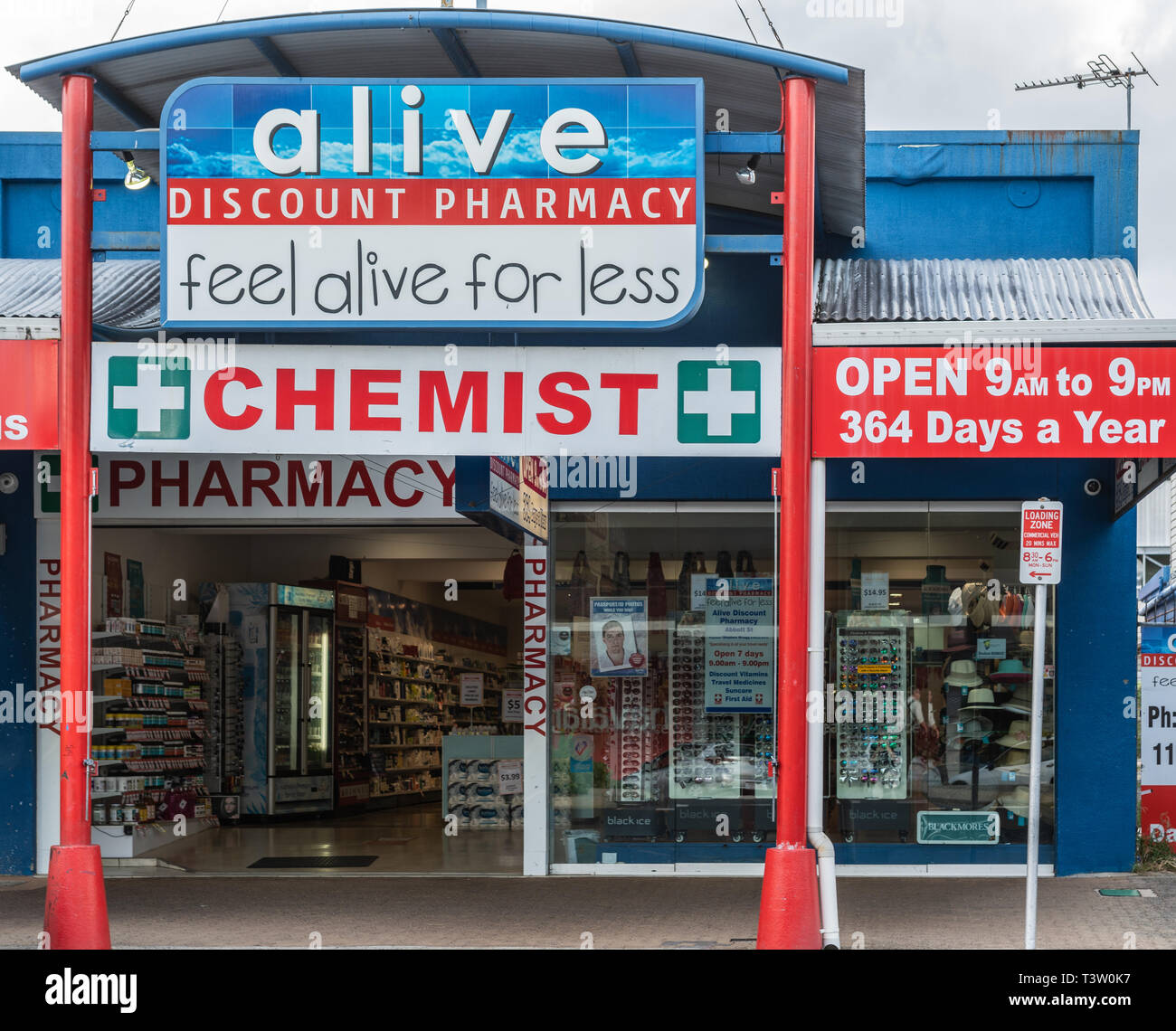 Cairns, Australia - February 17, 2019: Pharmacy and Chemist business in Abbott Street features blue and red advertisements. Open doors and gray skies. Stock Photo