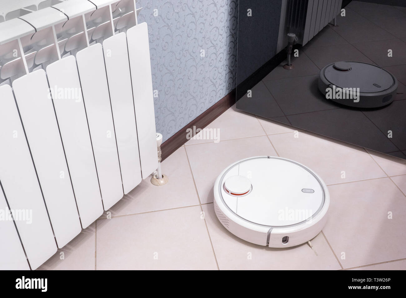 Robotic vacuum cleaner on laminate floor is reflected in mirror of fridge, smart home robotics wireless cleaning for simplify routine housework, effic Stock Photo
