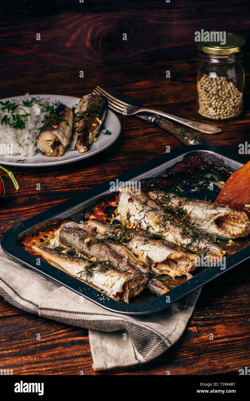 Baked fish carcasses on baking sheet over wooden surface Stock Photo