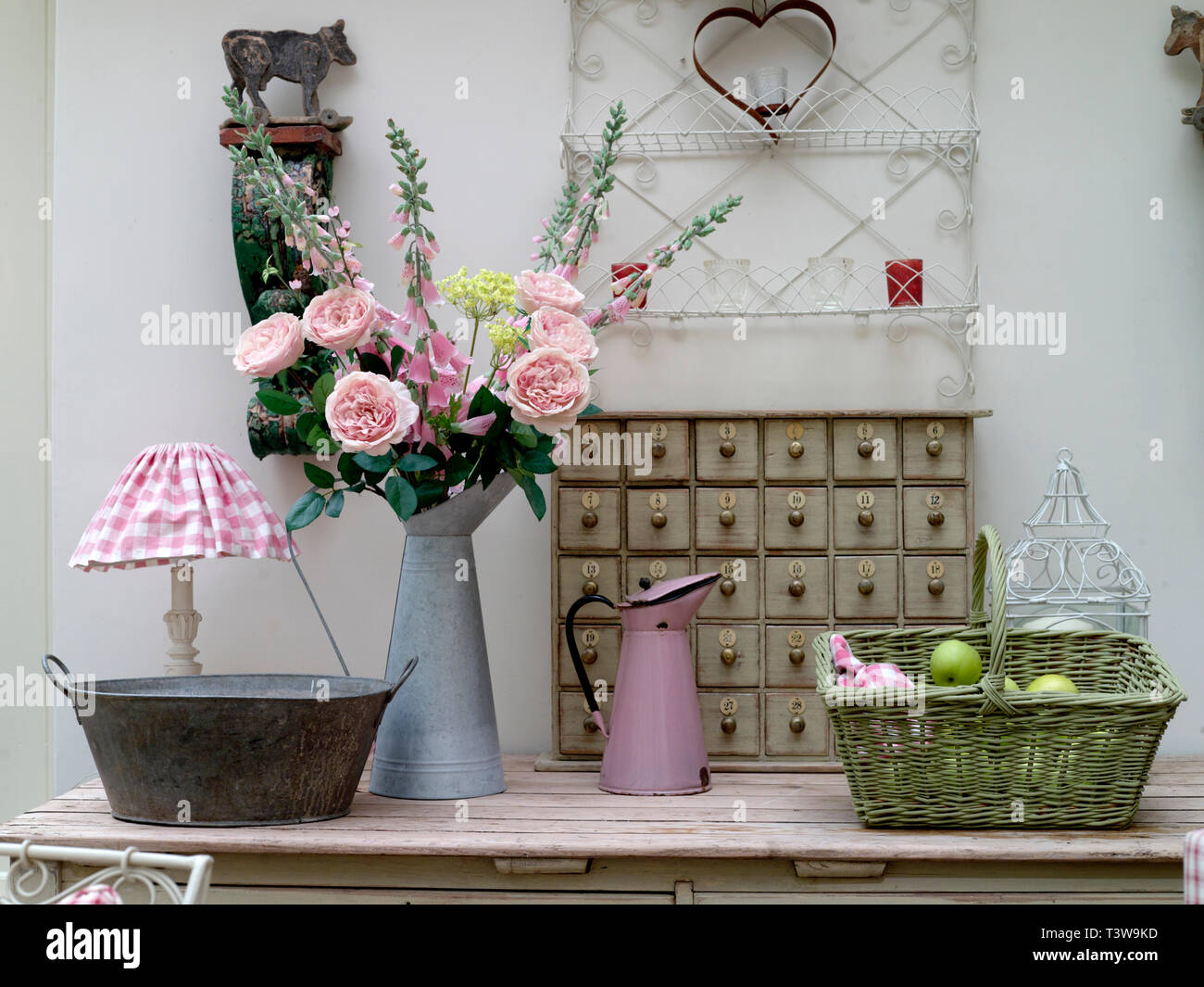 Country cottage look with roses, basket of apples and pink & white gingham lamp shade Stock Photo