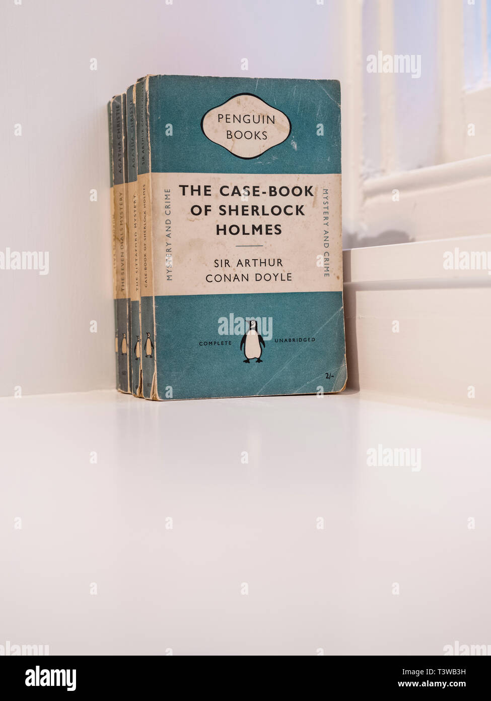 Old copies of The Case-book of Sherlock Holmes by Arthur Conan Doyle published by Penguin sitting on a white shelf. Stock Photo